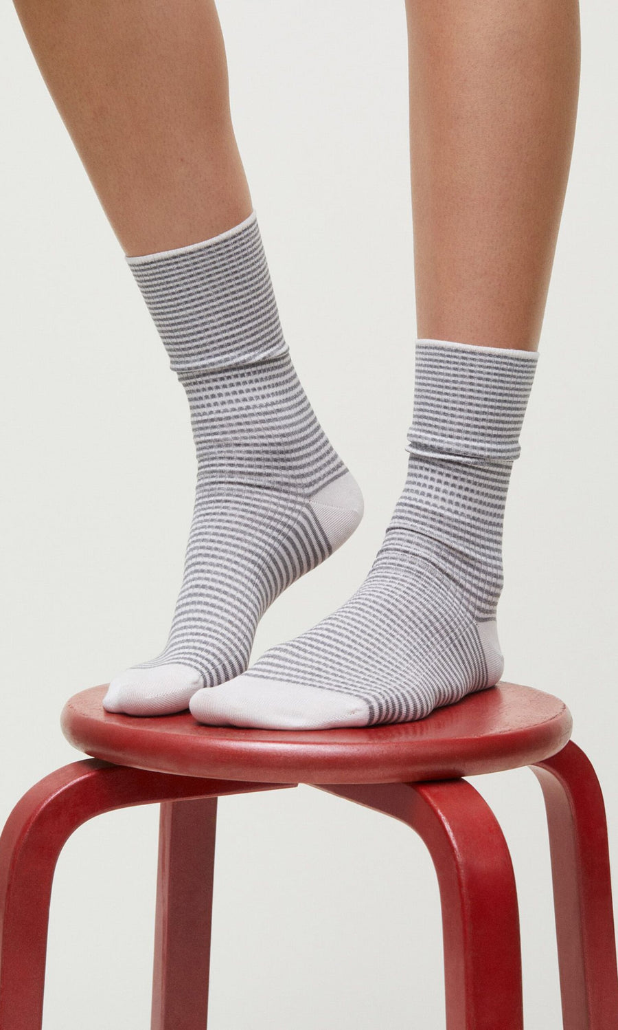 Plümo- Person wearing Grey Stripe Socks stands on a red stool against a plain background.