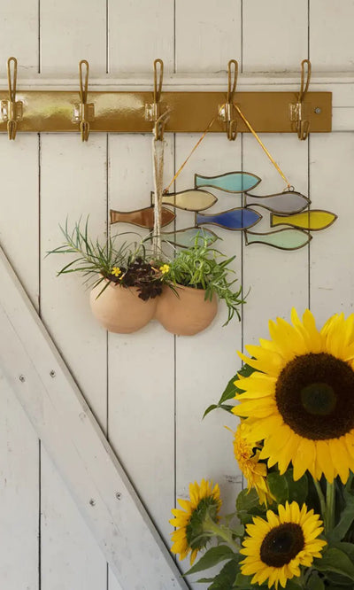 Plümo- A Shoal of Fish Mobile hangs above sunflowers next to a painted glass wall on a white wooden wall.