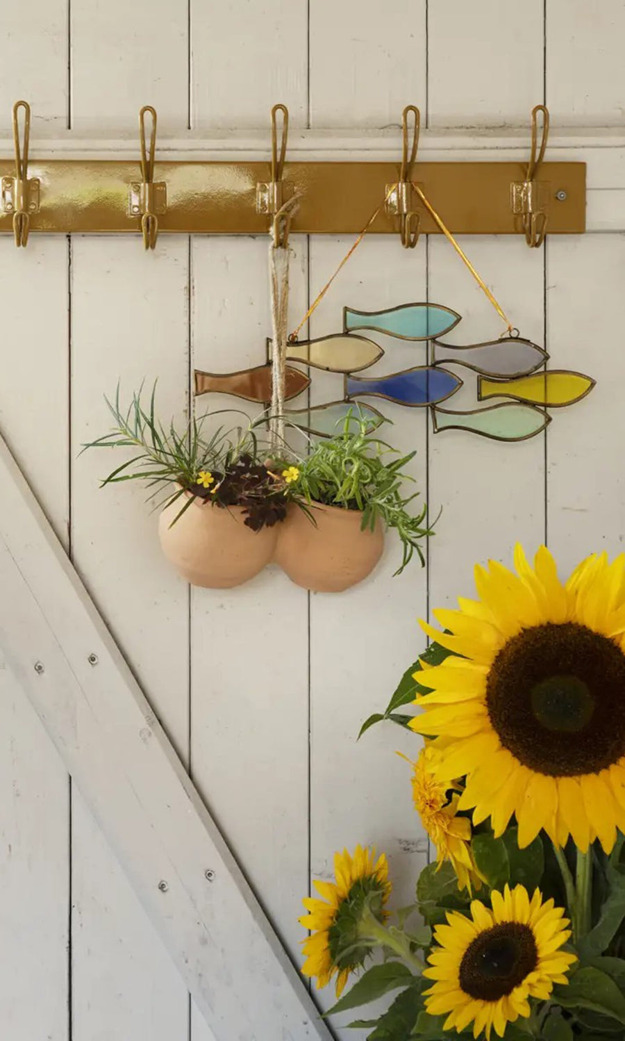 Plümo- A Shoal of Fish Mobile hangs above sunflowers next to a painted glass wall on a white wooden wall.