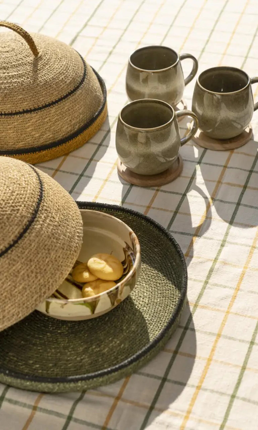 Plümo- Three mugs and cookies on a checkered cloth with a Seagrass Food Cover, adding rustic charm to your home decor.