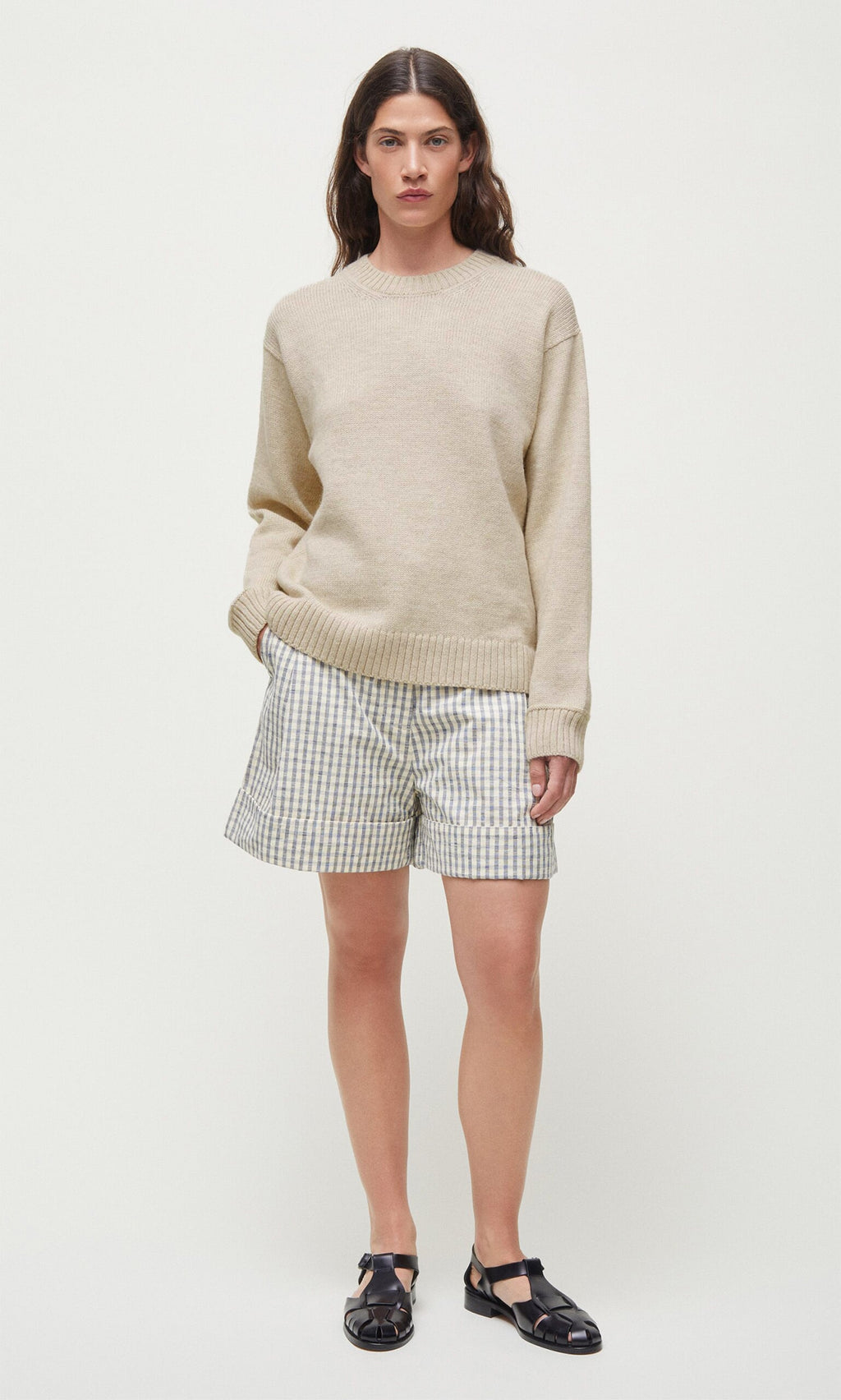 Plümo- A person wears the beige Christie Wool Jumper with plaid shorts and black sandals against a plain white background.