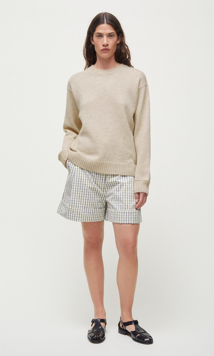 Plümo- A person wears the beige Christie Wool Jumper with plaid shorts and black sandals against a plain white background.