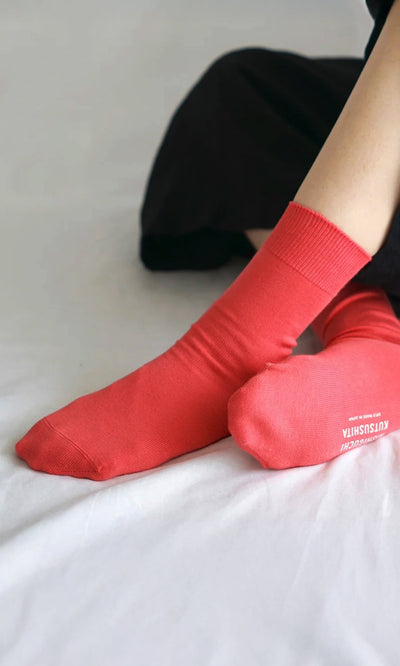 Plümo- Someone wearing Japanese Red Socks sits on a white surface with their legs slightly crossed.