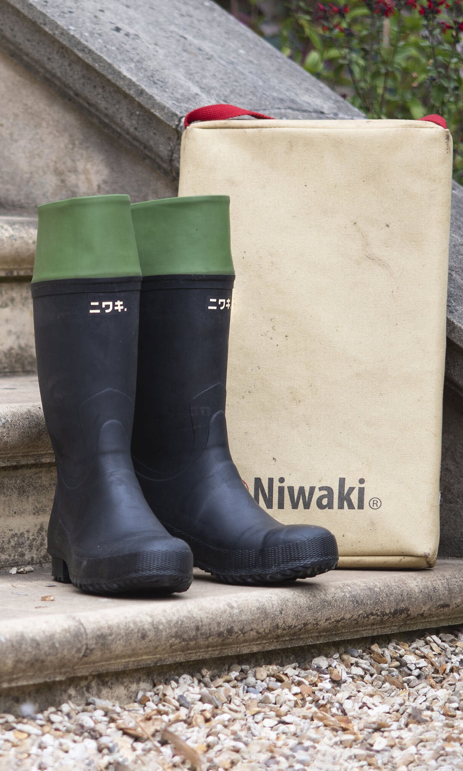 Plümo- Black and green Niwaki wellingtons with steel toes sit by a beige Niwaki bag on stone steps with Japanese text.