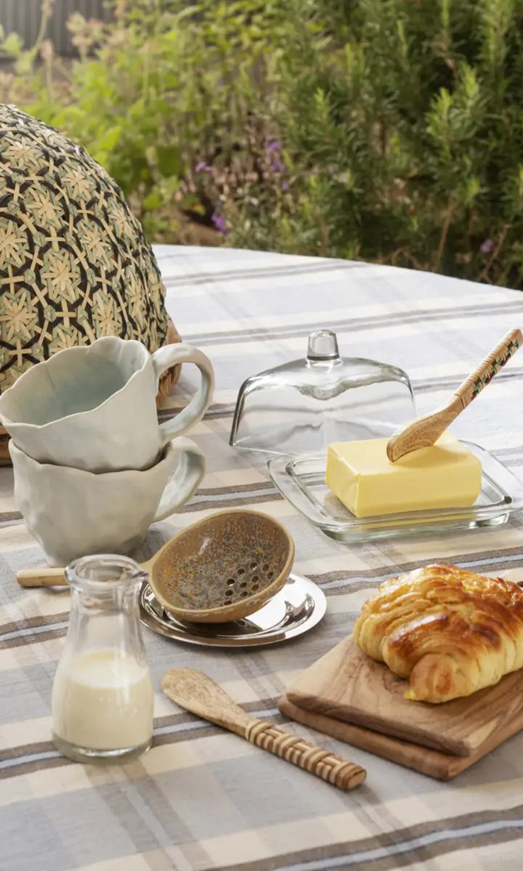 Plümo- A table set with croissant, butter, milk, and a handmade Serving Spoon on a checkered tablecloth outdoors.