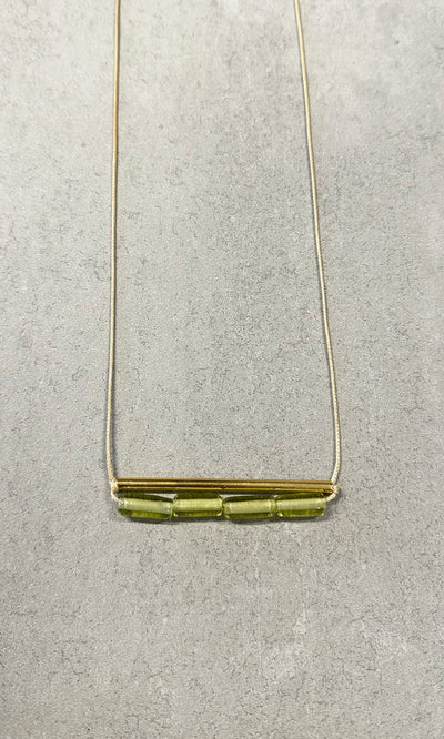 Plümo- The Lydia Necklace: a green beaded necklace with a gold bar and three glass beads on a light gray textured background.
