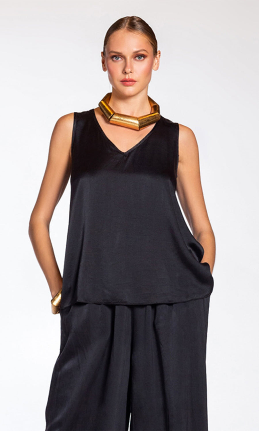 Plümo- Woman wearing the Carmen Top - Silk, paired with pants and chunky gold jewelry, hands in pockets.