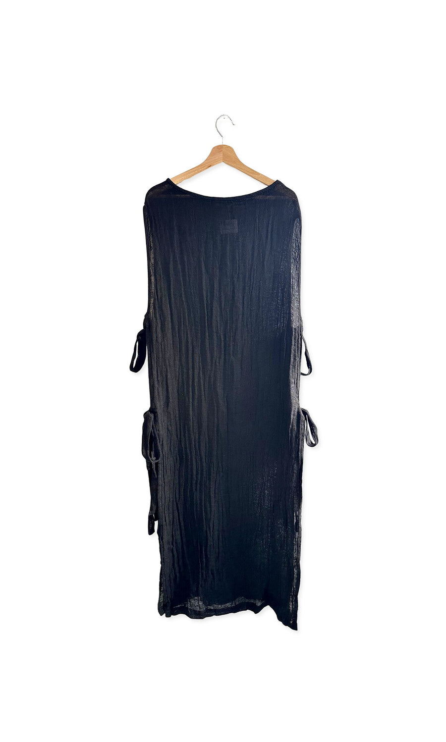 Plümo- The Lydia Linen Tabbard, a long black sheer dress with side ties, hangs on a wooden hanger against a white background.