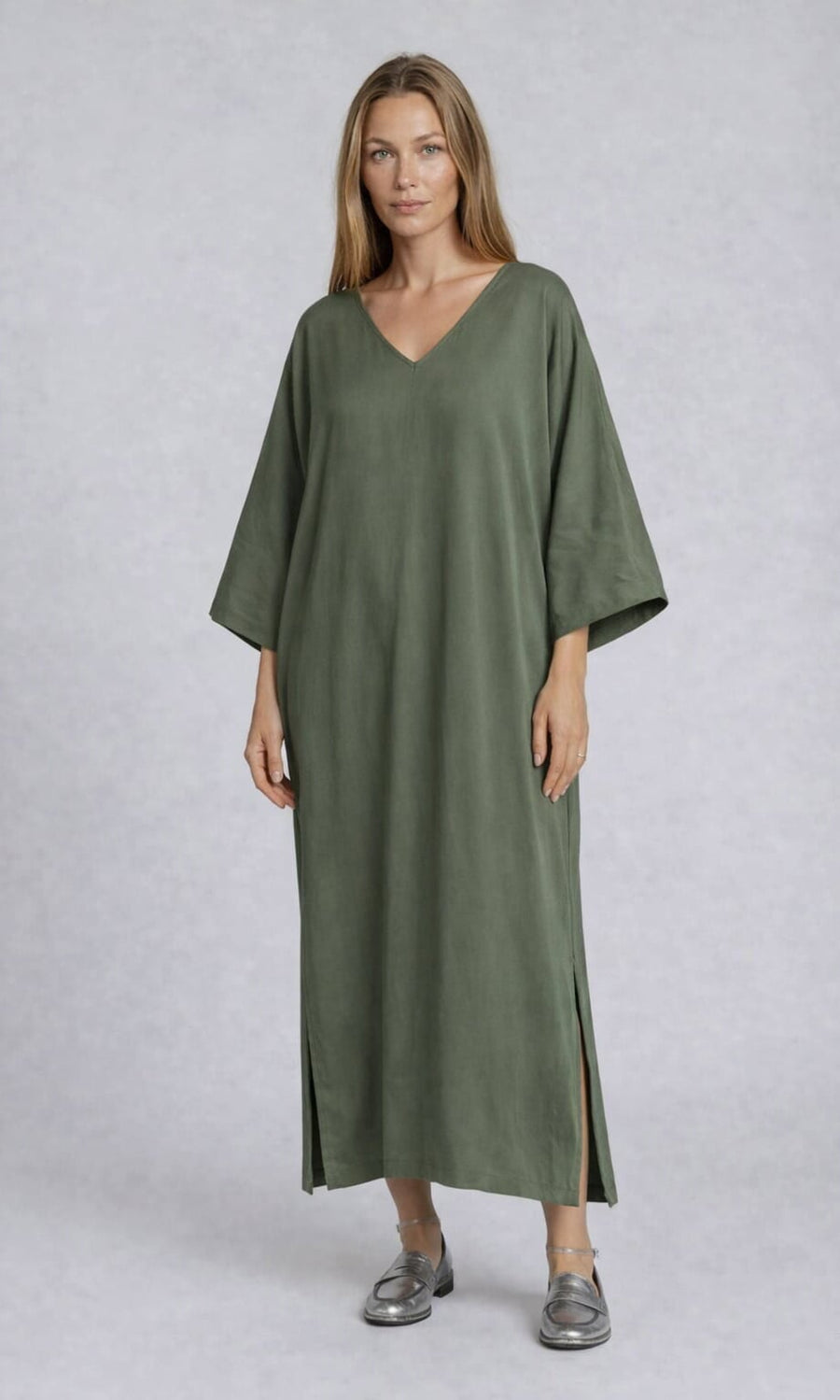 Plümo- Woman in the Novelle Dress—an oversized, olive green V-neck with half sleeves—paired with silver loafers.