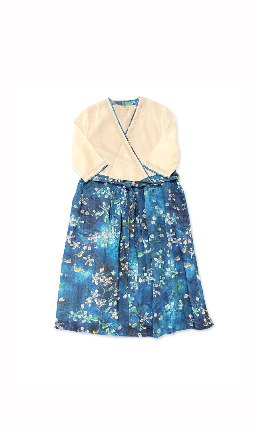 Plümo- The Quing Floral Dress is a children’s wrap dress with a cream top and blue floral skirt, one size fits most.
