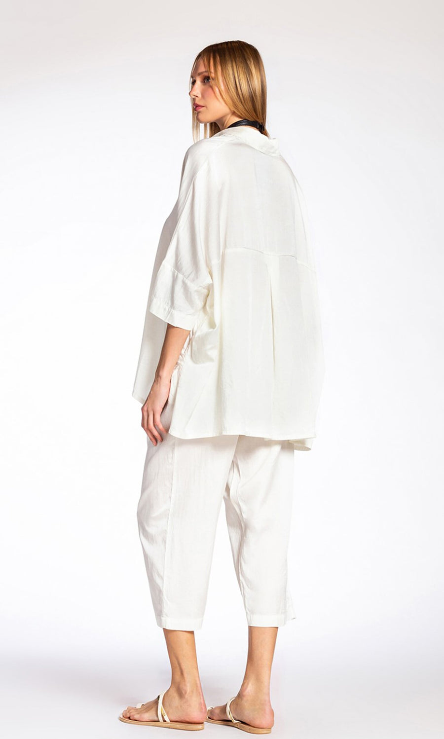 Plümo- Woman in a loose white shirt and Serina Silk Pants, wearing sandals, standing sideways.