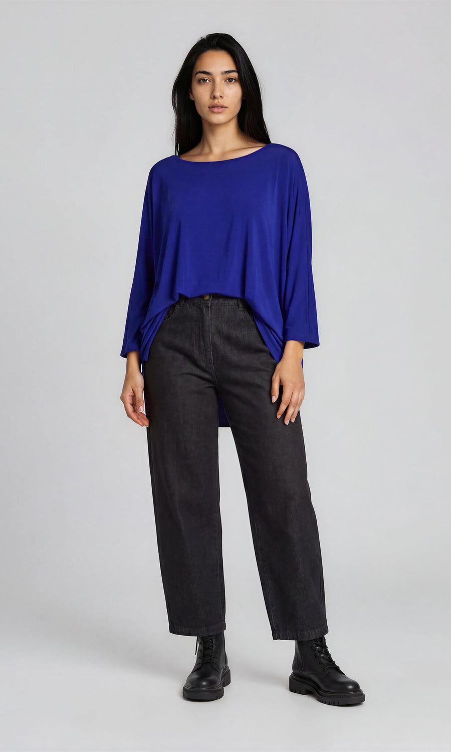 Plümo- Woman wearing a relaxed fit Yara Top in royal blue, black jeans, and boots against a light gray background.