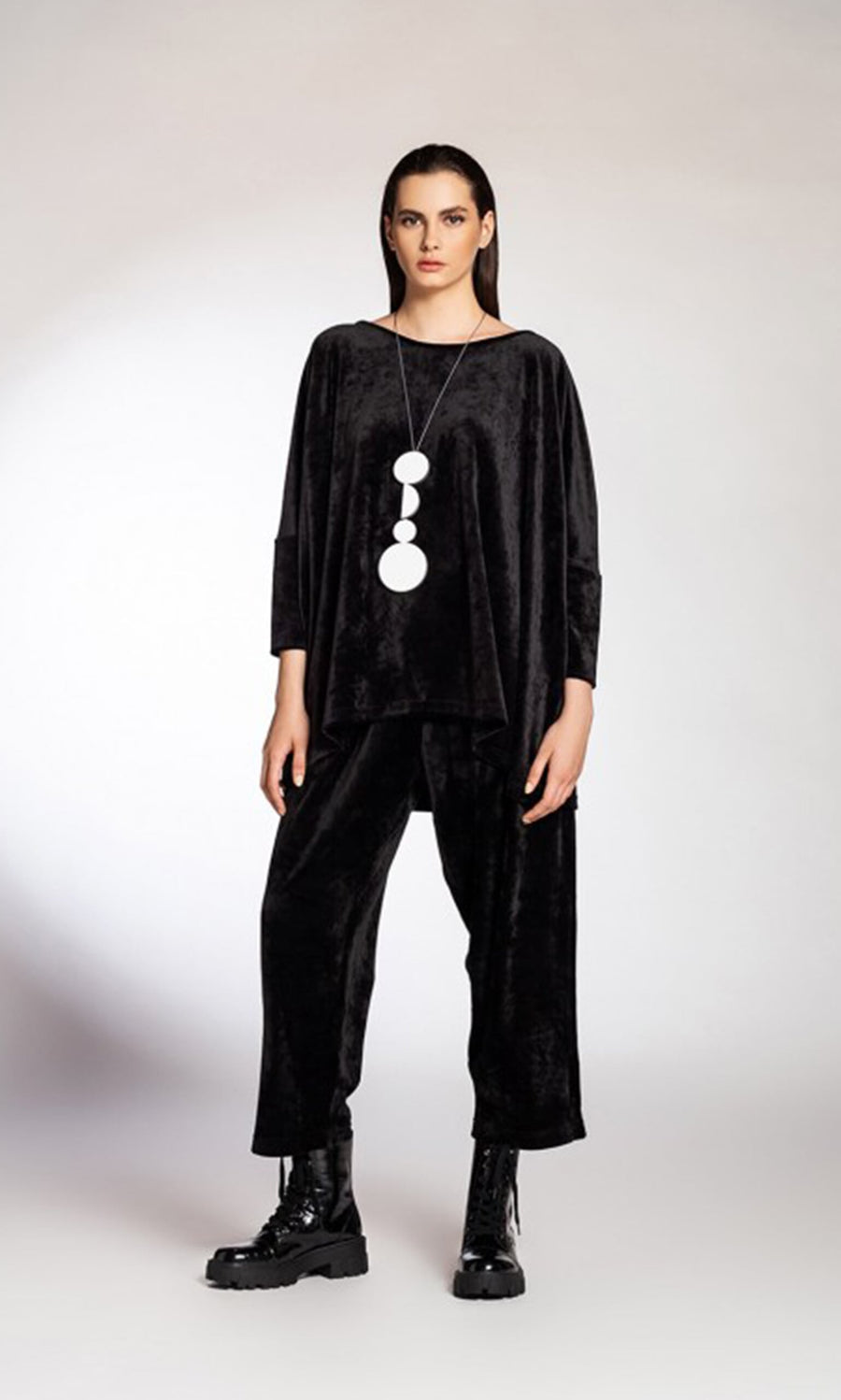 Plümo- Woman wearing the Zaria Top, a black velvet wide-neckline top, styled with chunky boots and a long pendant necklace.