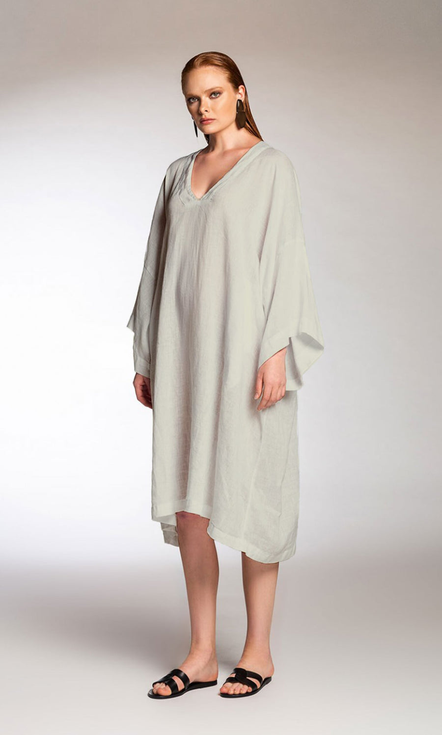 Plümo- Woman wearing the Virelle Kaftan Dress, a relaxed-fit grey long dress with wide sleeves, and black sandals.