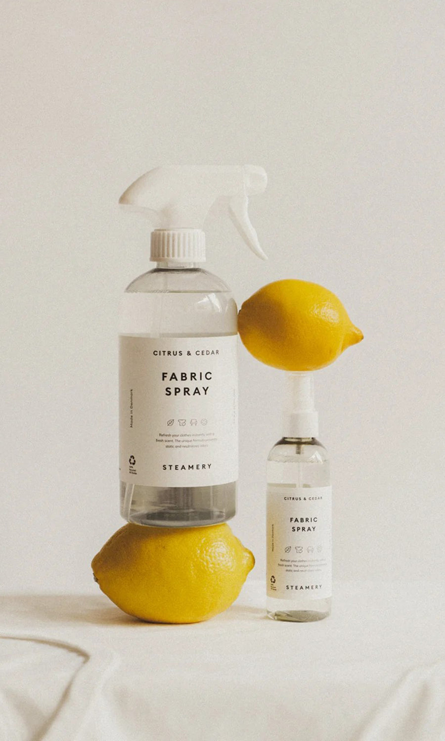 Plümo  Two lemons and two bottles of Citrus  Cedar Fabric Spray on a white surface with a plain background.