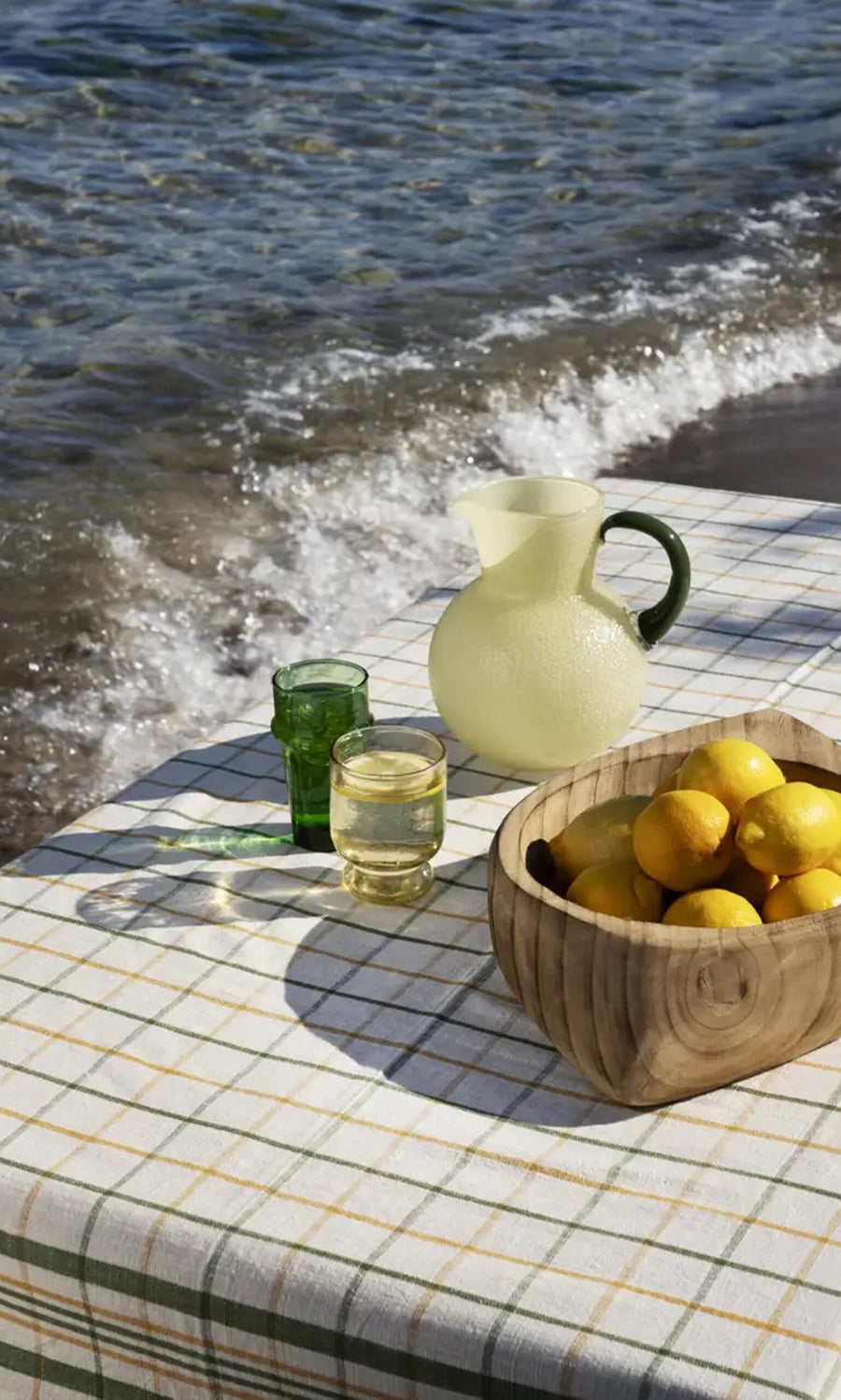 Plümo- A table by the sea with a pitcher, two glasses, lemons, and a Farmhouse Table Cloth.