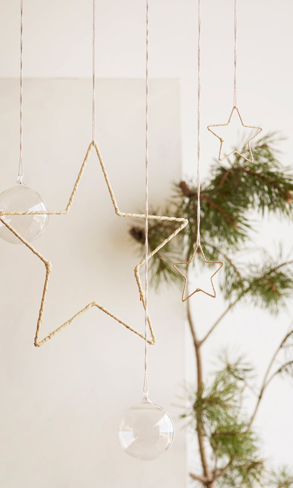 Plümo- Minimalist holiday decor featuring a handmade Raffia Christmas Star ornament and glass baubles by pine branches.