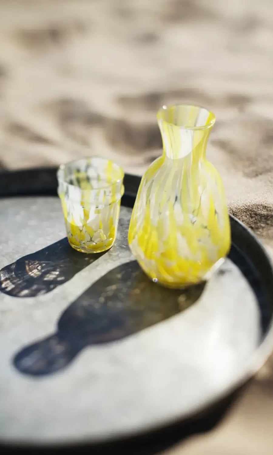 Plümo- Speckled Glass Jug - Yellow, handmade from recycled glass, on a metal tray casting shadows in sunlight.